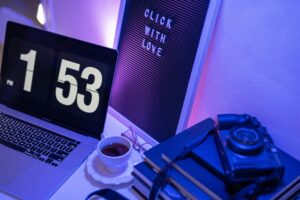 A modern workspace featuring a laptop, vintage camera, books, and a motivational sign.