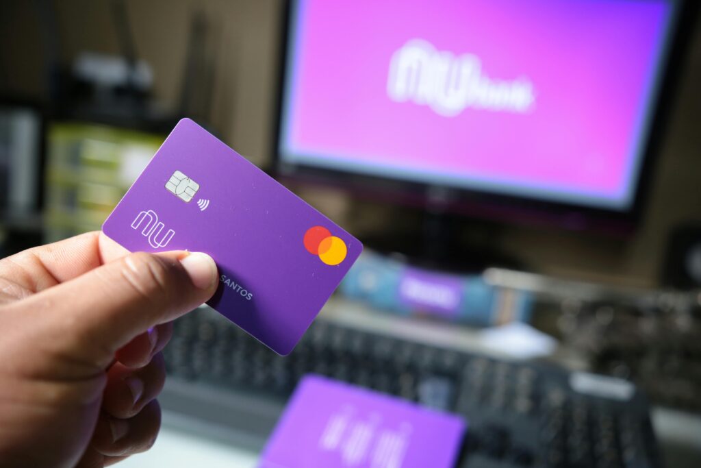 A close-up of a hand holding a purple bank card in front of a computer screen.