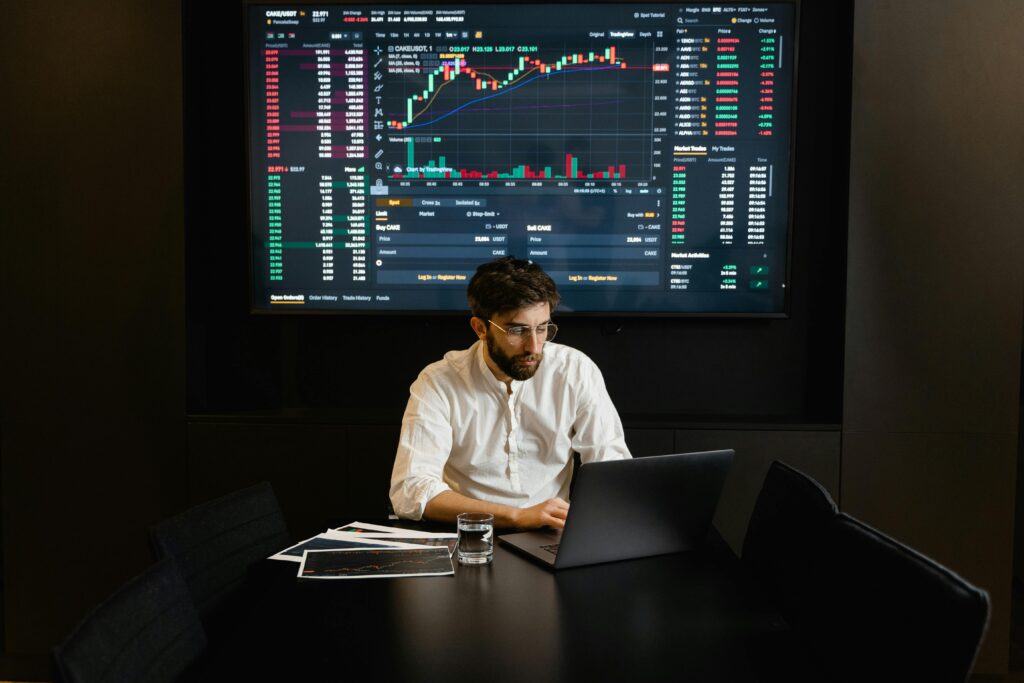 Focused businessman analyzing stock market data on laptop with financial graphs displayed on screen.