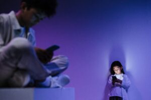 Two kids focusing on their smartphones in a dimly lit studio environment.